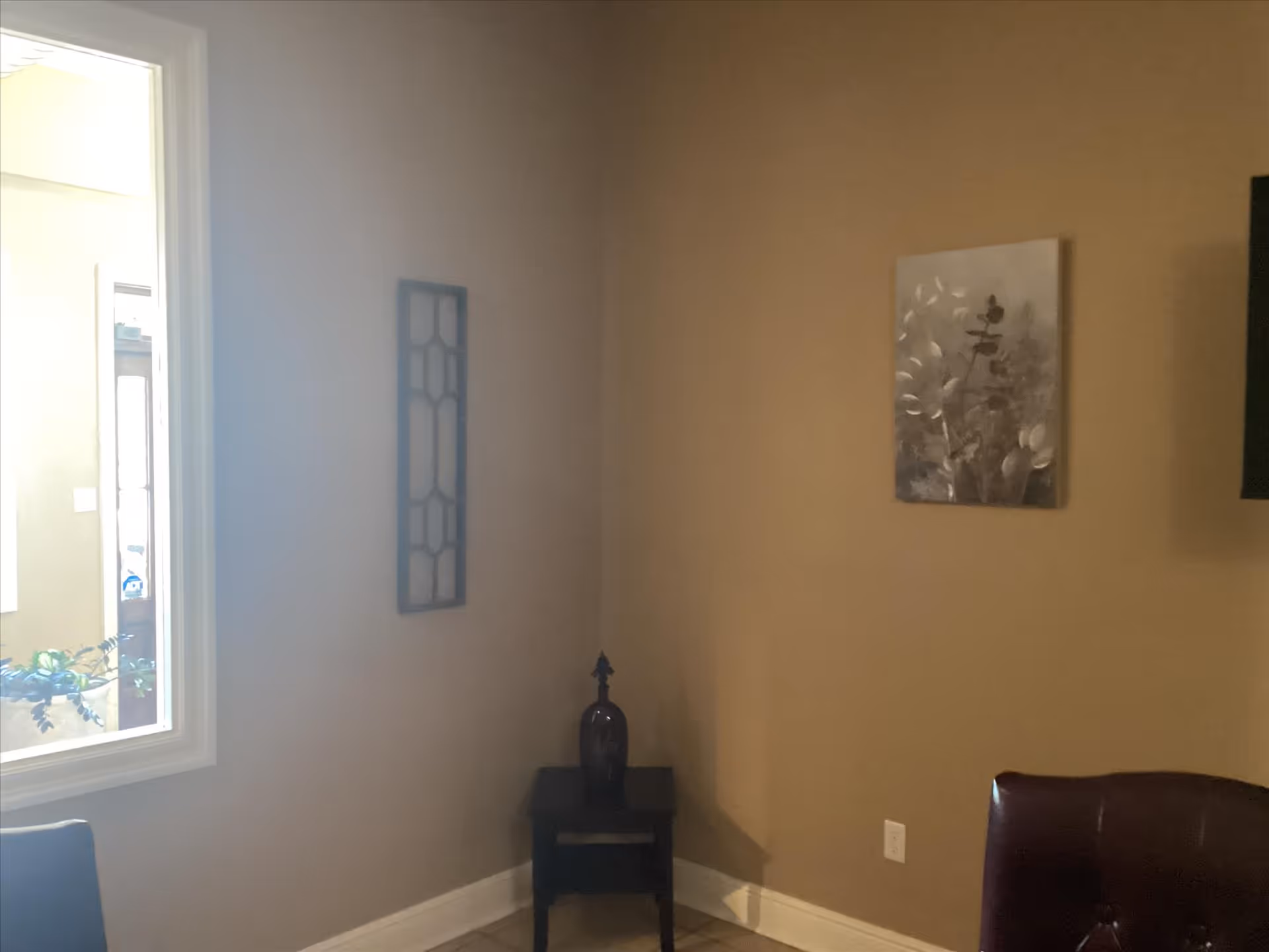 Interior corner of a living area with wall art, small table, and vase.