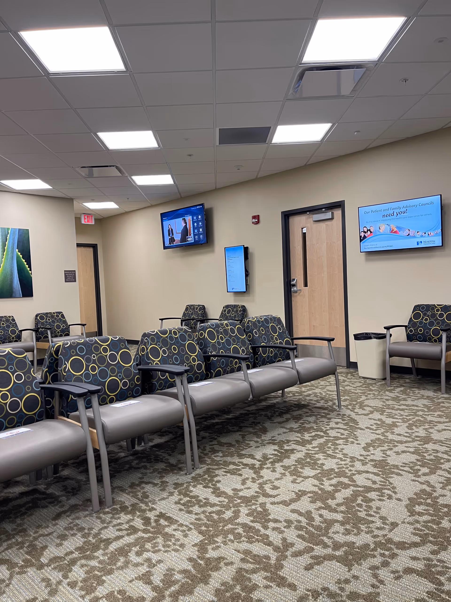 Waiting area of Norton Healthcare Medical Plaza III Brownsboro with patterned chairs and TVs.
