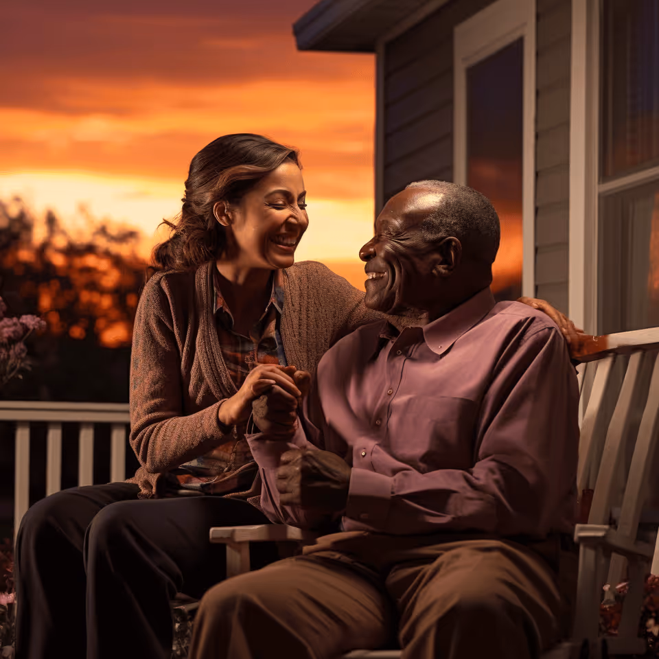 Two smiling adults sit on a porch bench at sunset, enjoying each other's company.