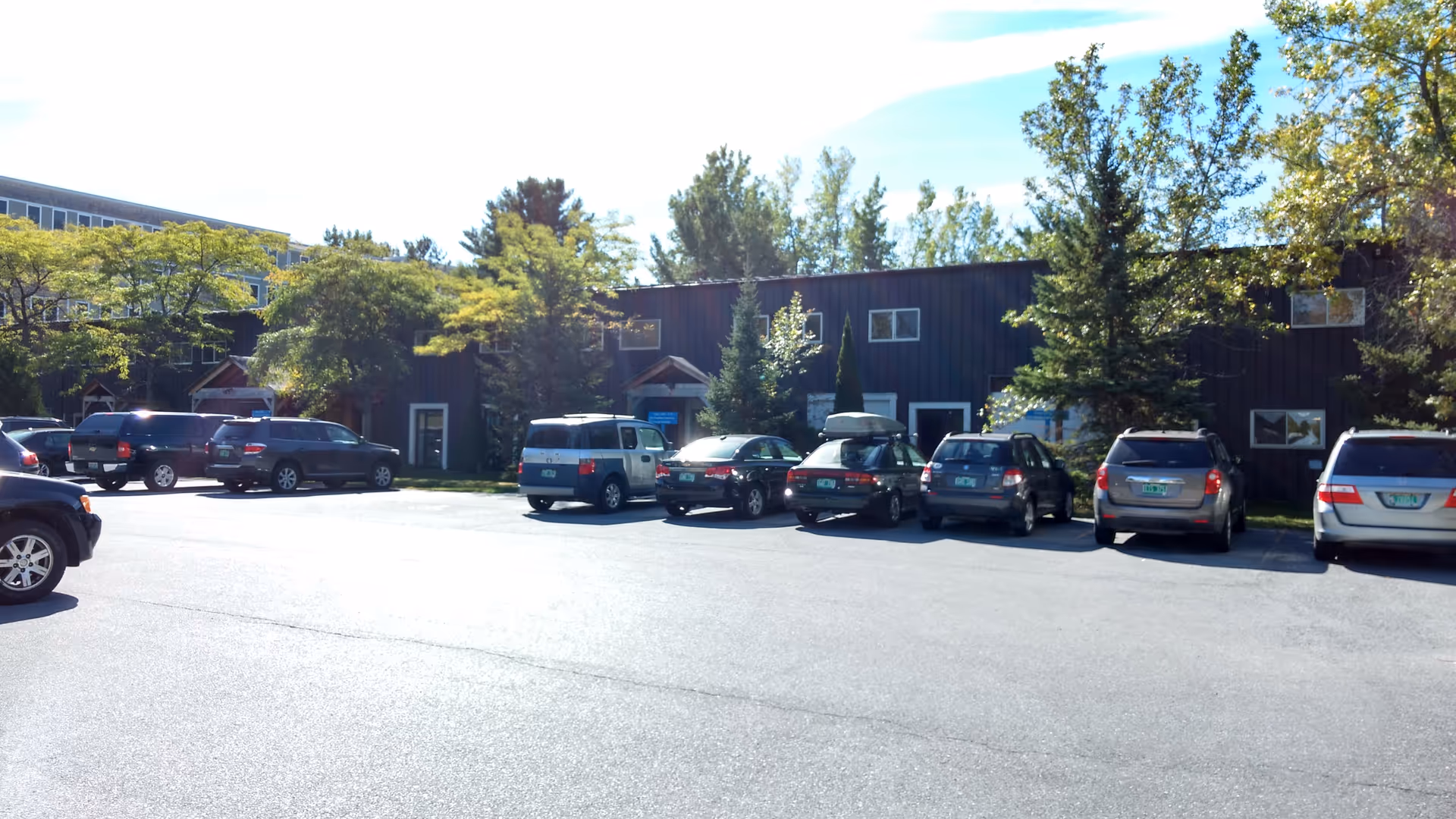 Parking lot in front of a dark building with trees and several parked cars.