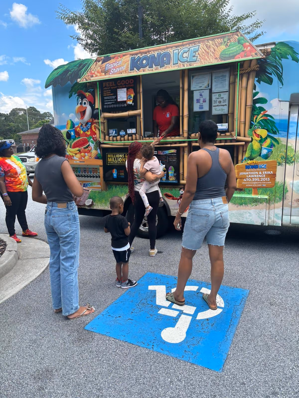 People gather around a colorful Kona Ice truck outdoors.
