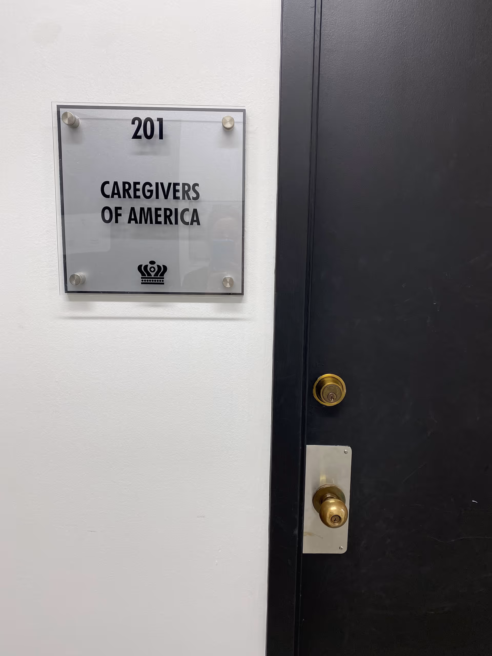 Door beside a plaque reading CAREGIVERS OF AMERICA, room 201, in a neutral interior hall.
