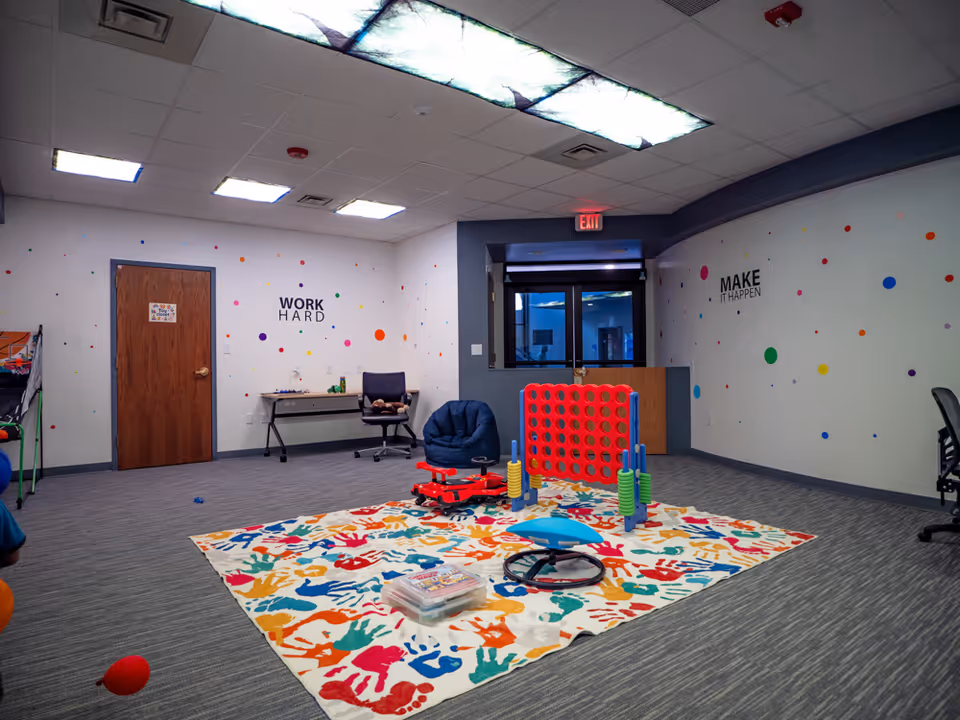 Colorful indoor therapy playroom with a mat, toys, and seating.