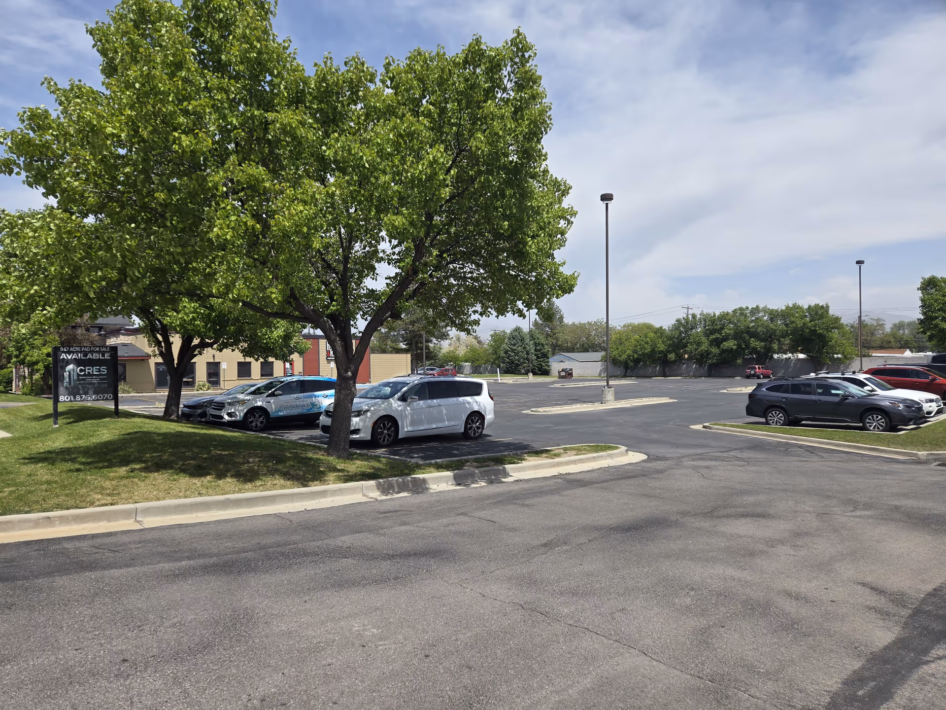 Exterior parking lot with several cars and green trees near a building.