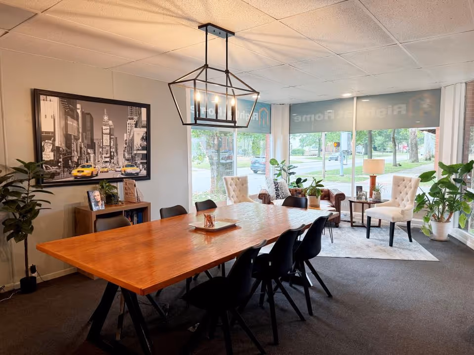 A spacious dining area with a large wooden table, black chairs, and potted plants.