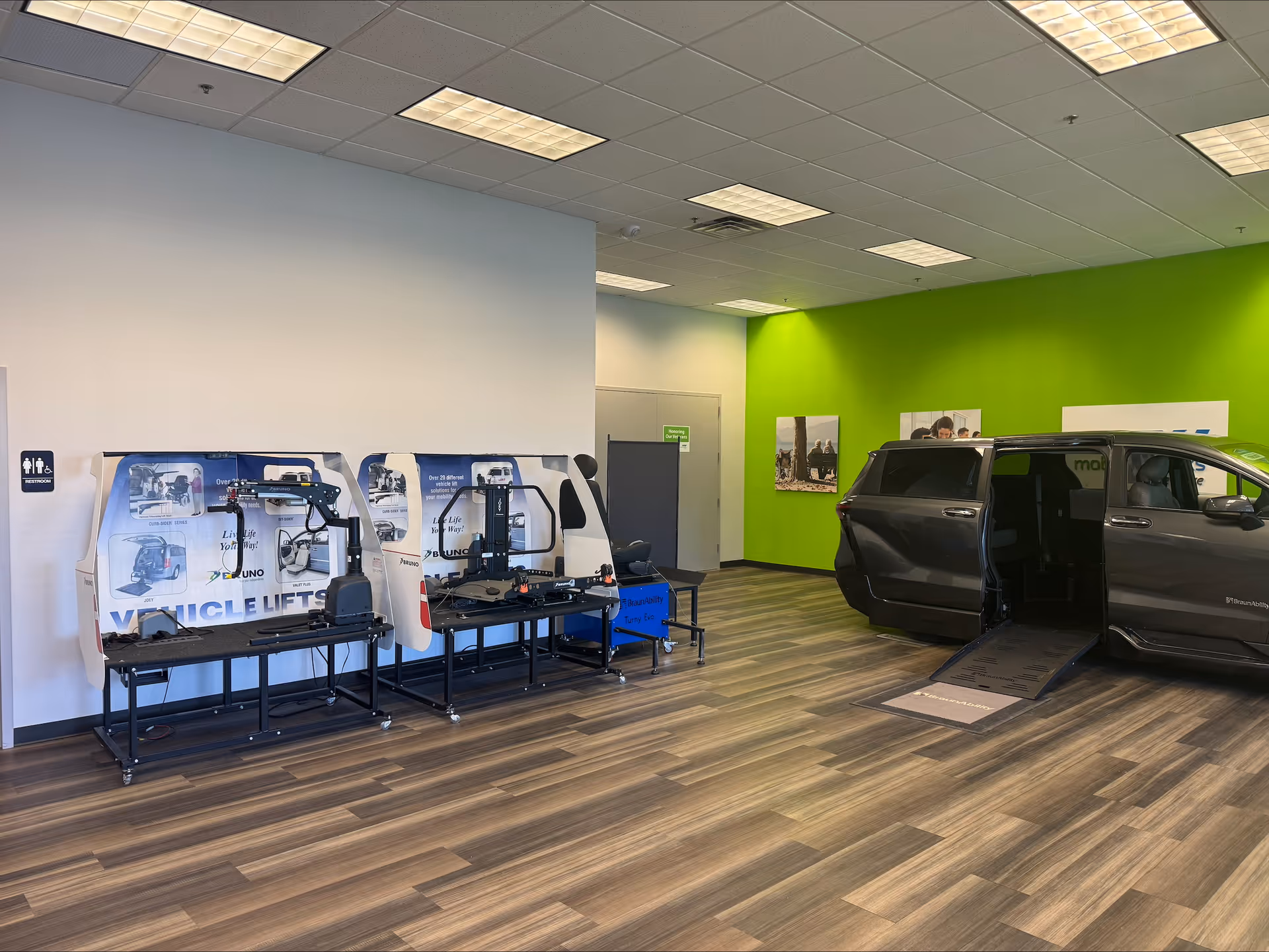 Indoor showroom with accessible van and wheelchair lifts, green accent wall, laminate flooring.
