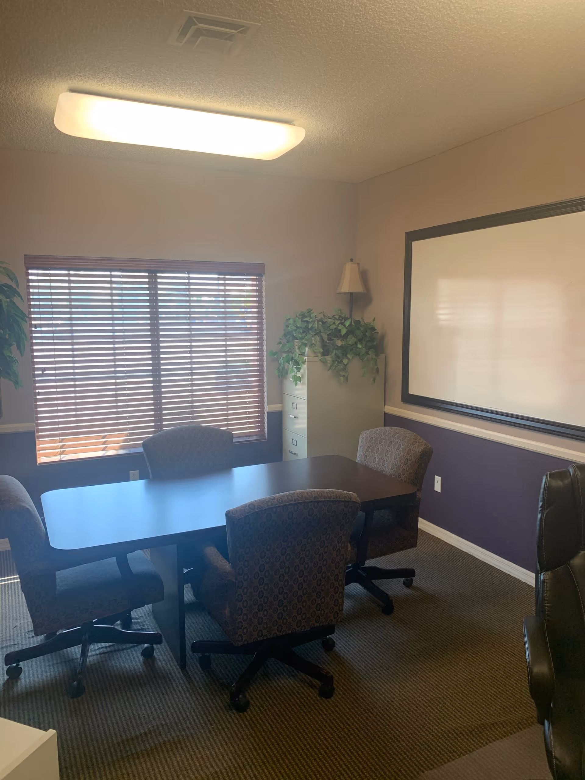 Interior meeting room with a rectangular table, chairs, a whiteboard, and potted plants.
