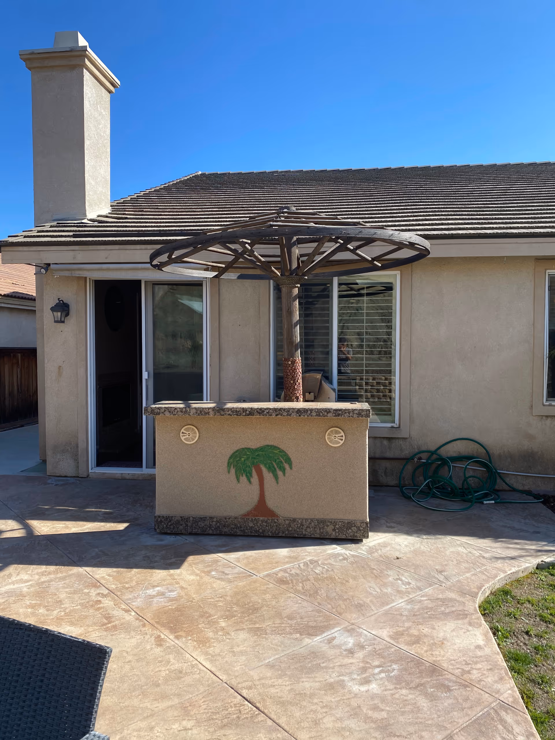 Backyard patio with built-in grill island and circular canopy against a beige house.