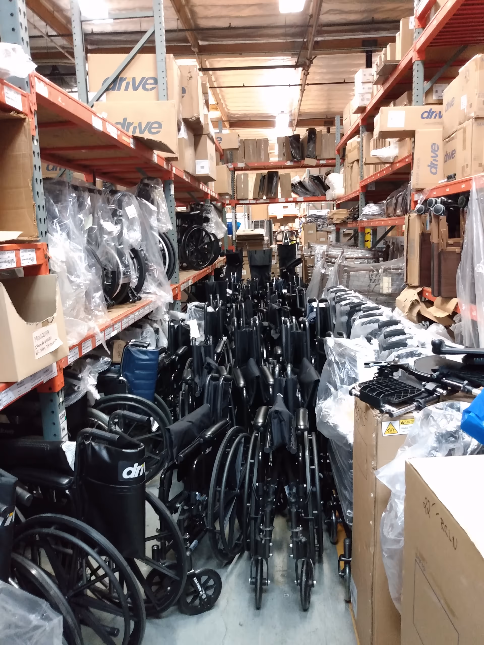 Narrow warehouse aisle filled with stacked wheelchairs and medical equipment.