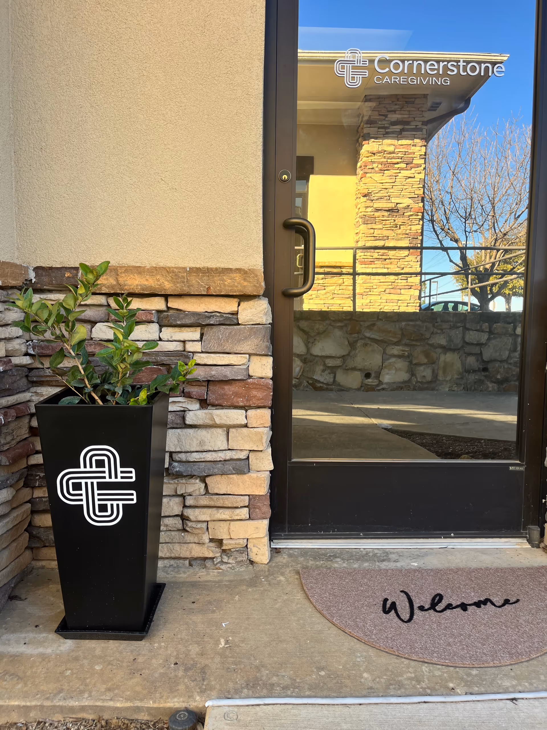 Exterior view of Cornerstone Caregiving entrance with plant, stone facade, and welcome mat.