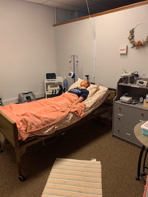 Patient rests in a hospital bed with pink blanket in a small care room.