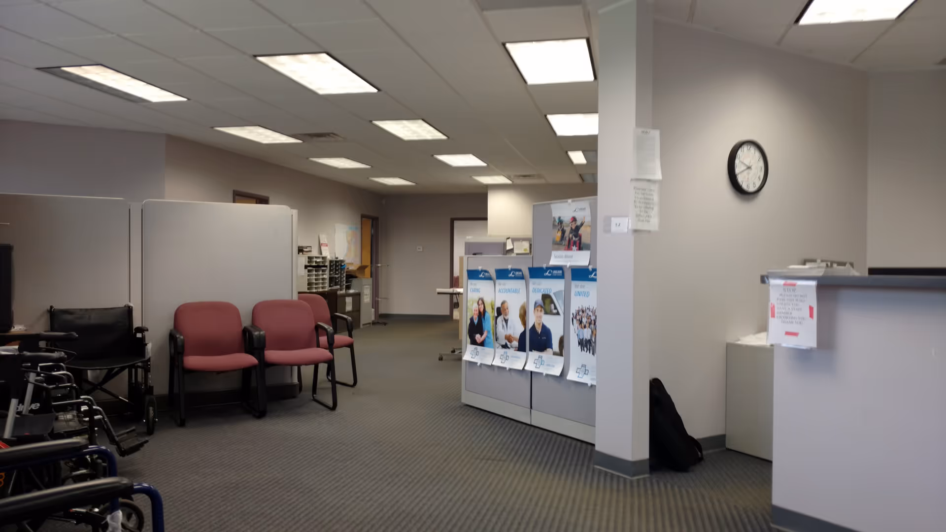 Interior lobby of LINCARE facility with pink chairs, posters, a reception desk, and a clock.
