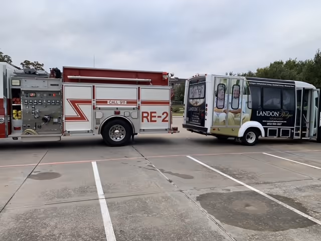 A fire truck parked beside a shuttle bus in a facility parking lot.