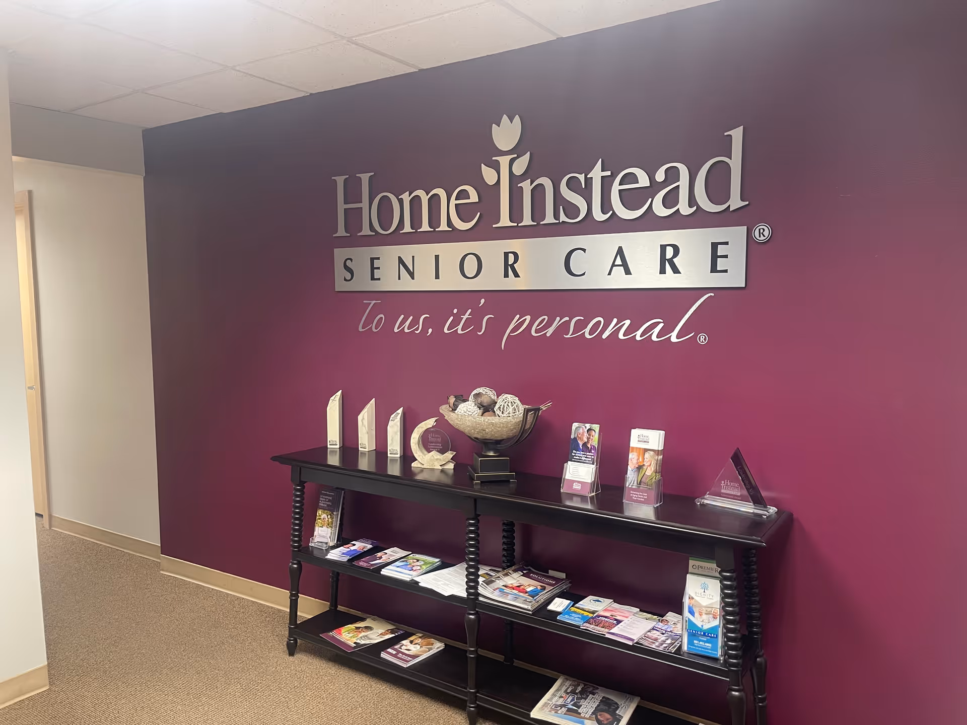 Interior lobby wall with Home Instead Senior Care sign and brochure table.