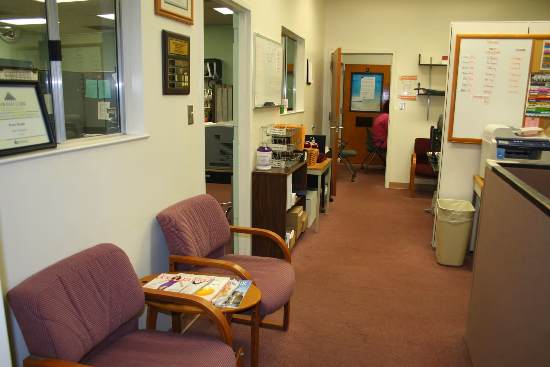 Waiting area with purple chairs, magazines, and a hallway leading to offices in a senior facility.
