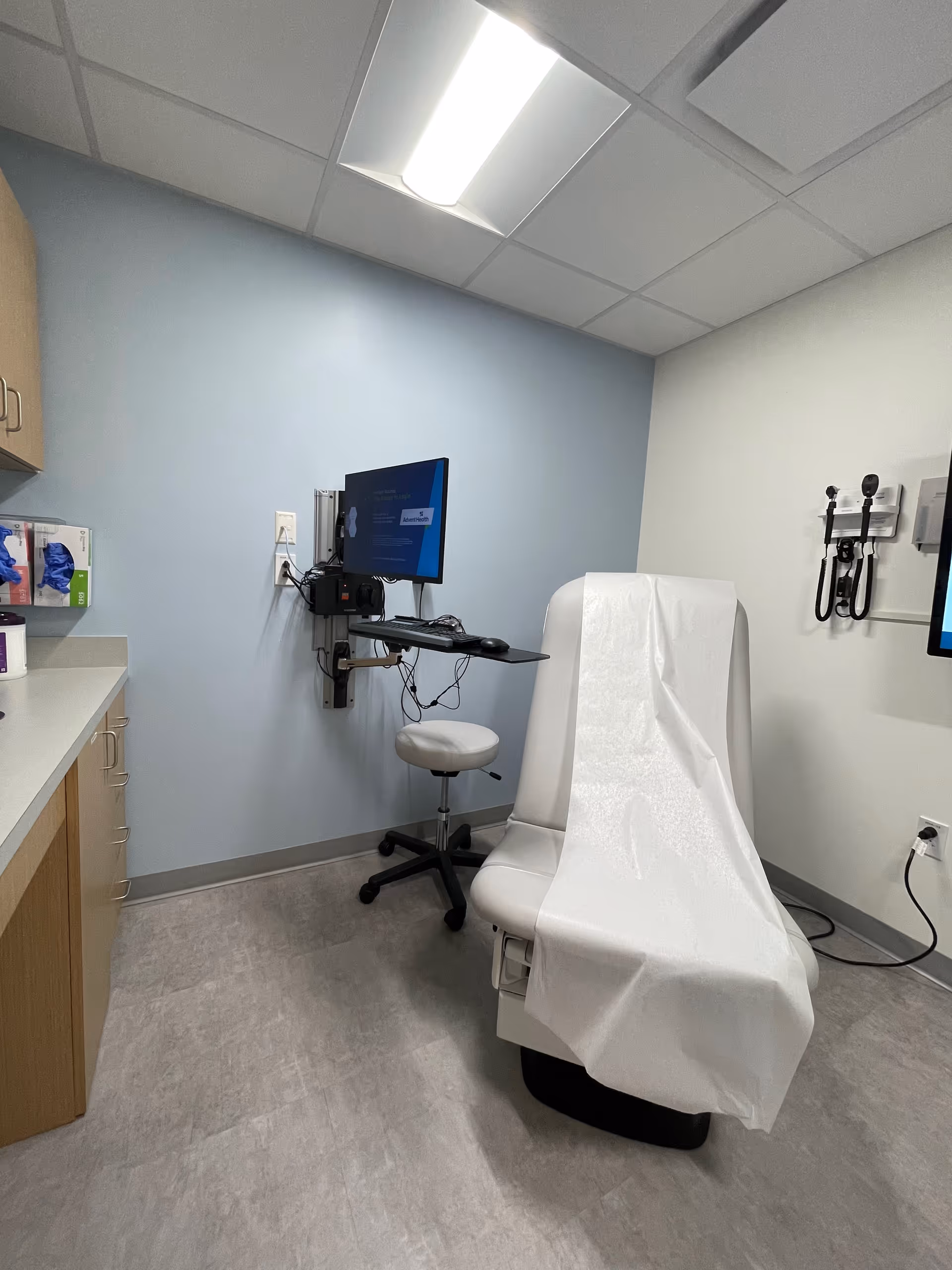 Medical exam room featuring a covered chair, monitor, and medical equipment.