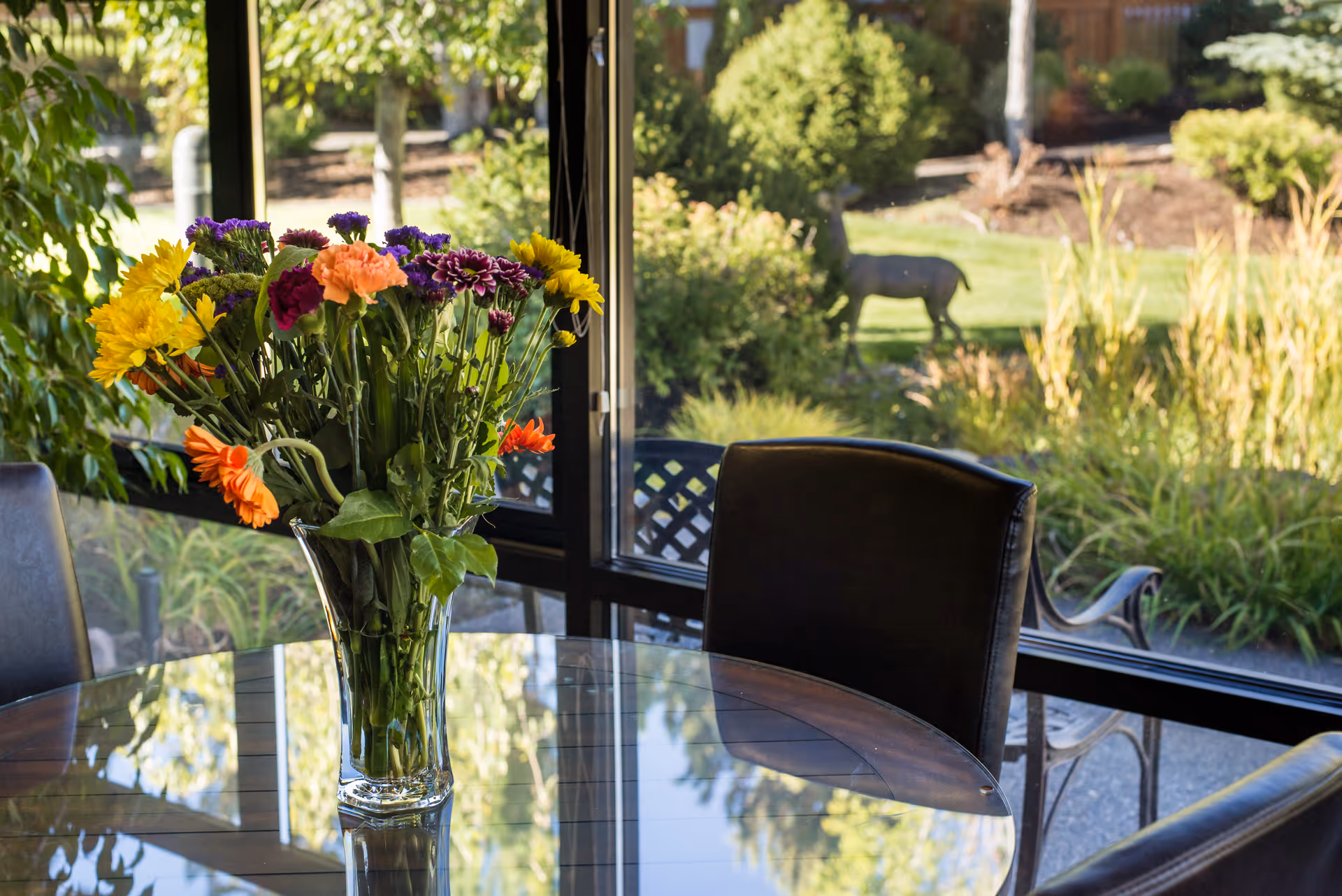 Interior dining area with glass table, colorful vase of flowers, and garden view outside.