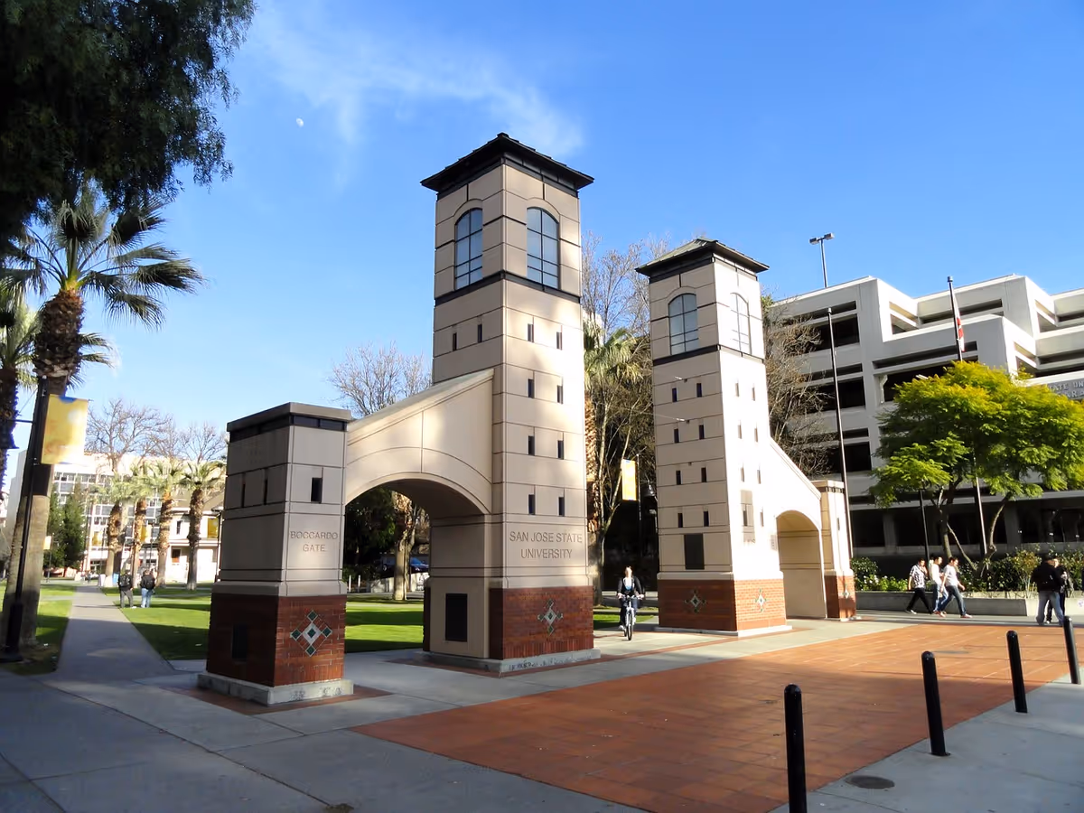 Tall beige gate towers frame a university campus entrance under a clear blue sky.