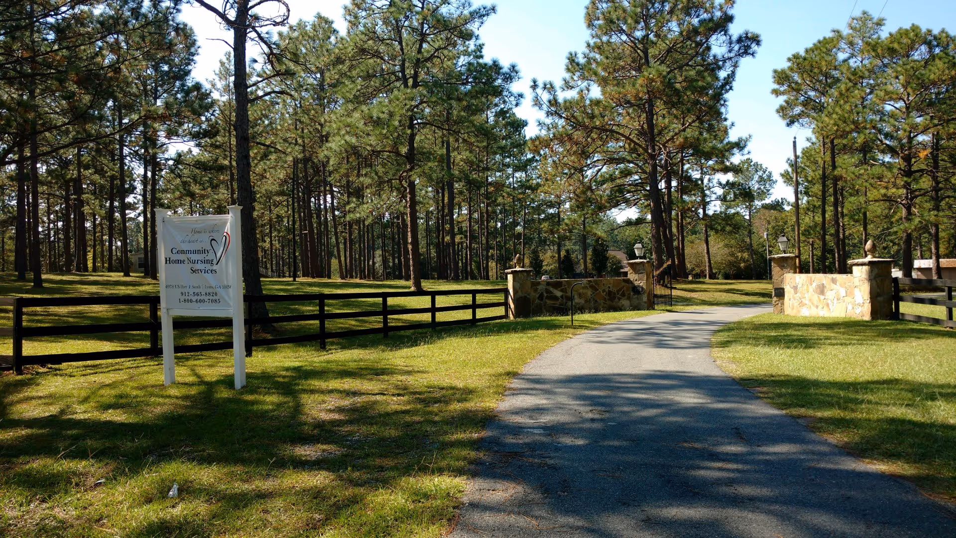 Winding paved path through grassy, tree-lined outdoor area by a facility sign.
