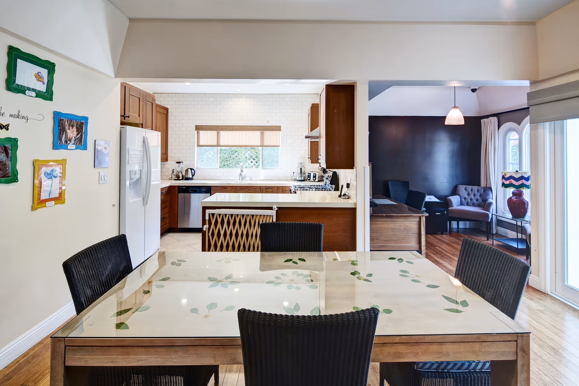 Open-concept dining area with a glass-top table, kitchen in back, and cozy living space.