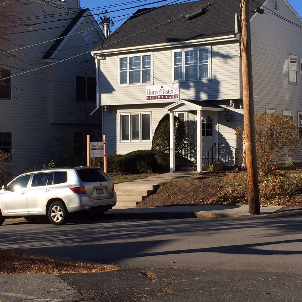Two-story Home Instead Senior Care building with sign, parked car, and street view.