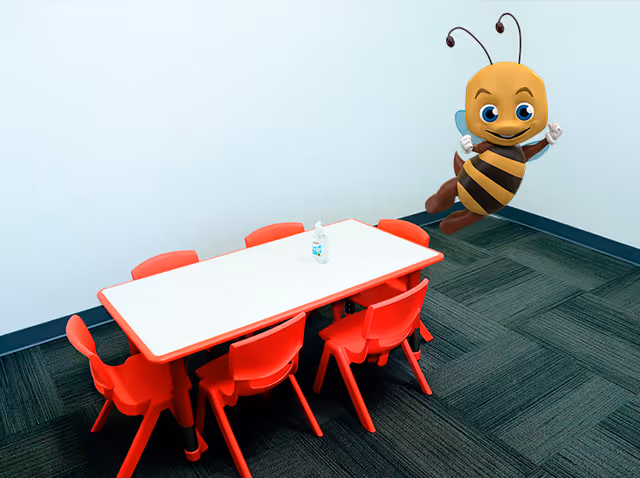 Small white table with red chairs in a bright interior, cartoon bee on the wall.