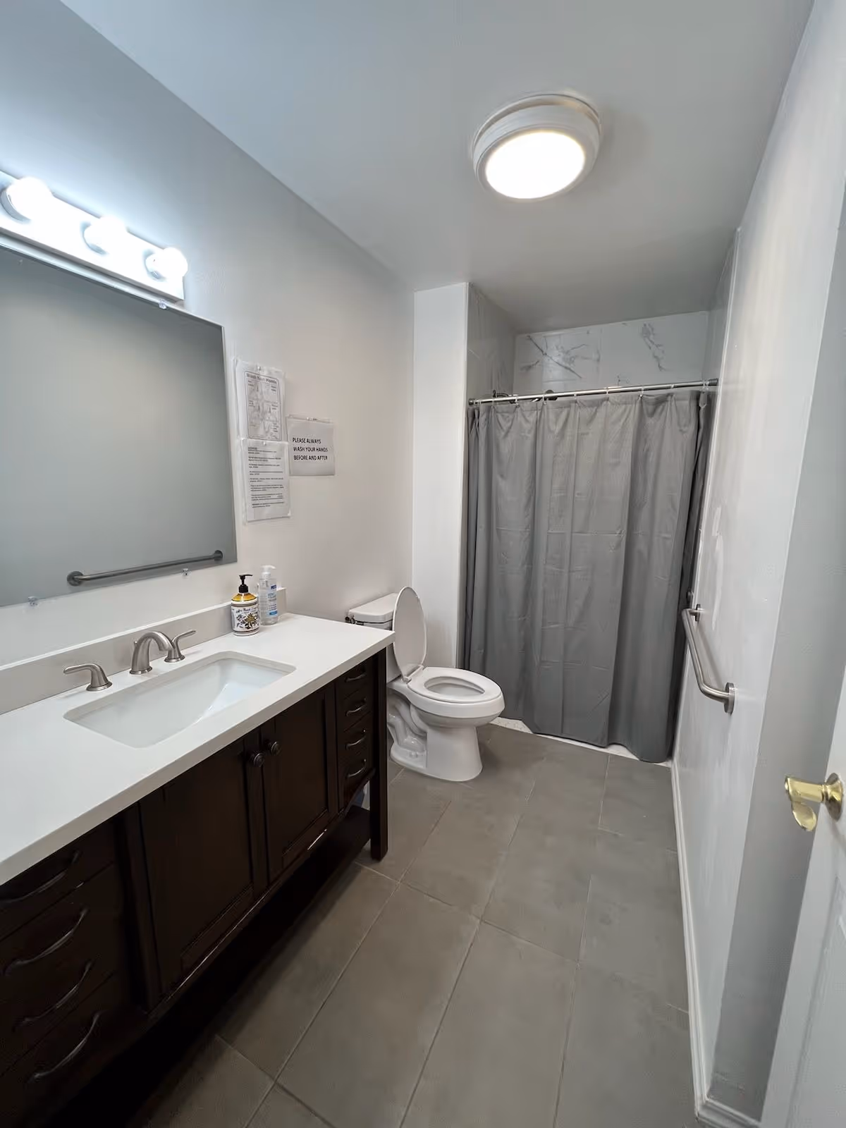 Bathroom with a dark wood vanity, single sink, mirror, toilet, and gray shower curtain.