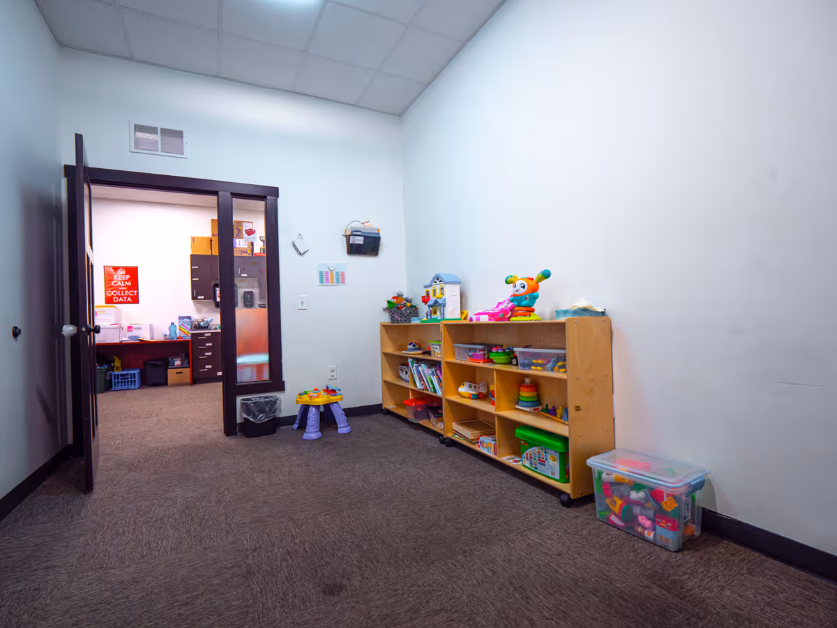 Playroom with toy shelves, colorful toys, and an open doorway to an office.
