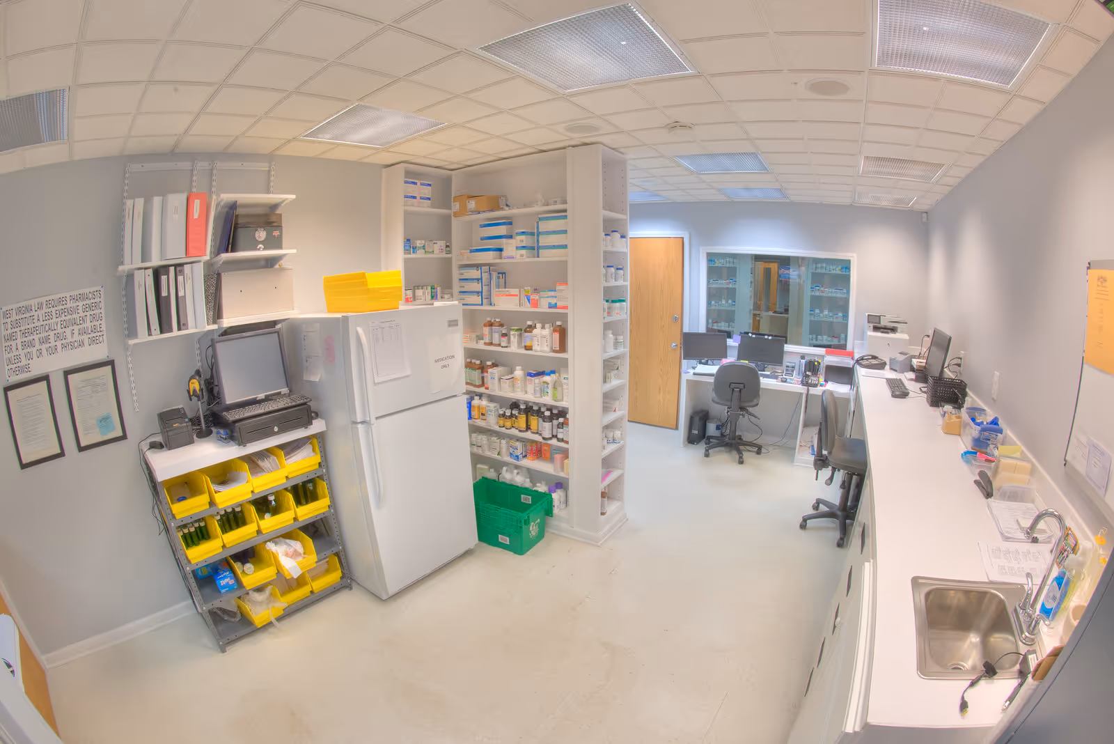 Well-lit medical supply room with shelves, a refrigerator, and a long counter with computers.
