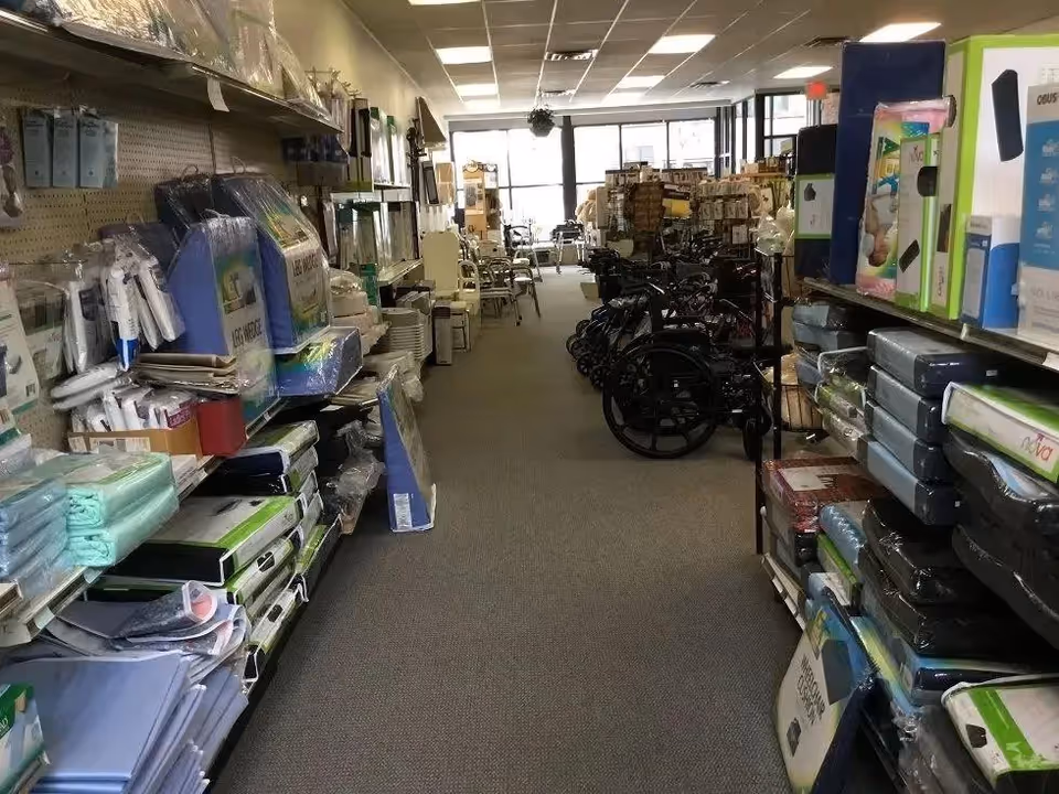 Narrow indoor supply aisle filled with medical equipment, boxes, and wheelchairs.