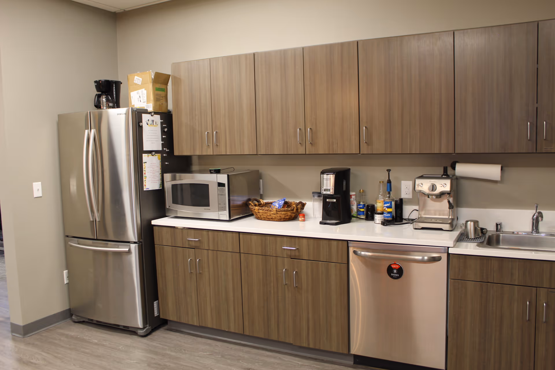 Senior living facility kitchen with fridge, microwave, coffee station, dishwasher, and sink.