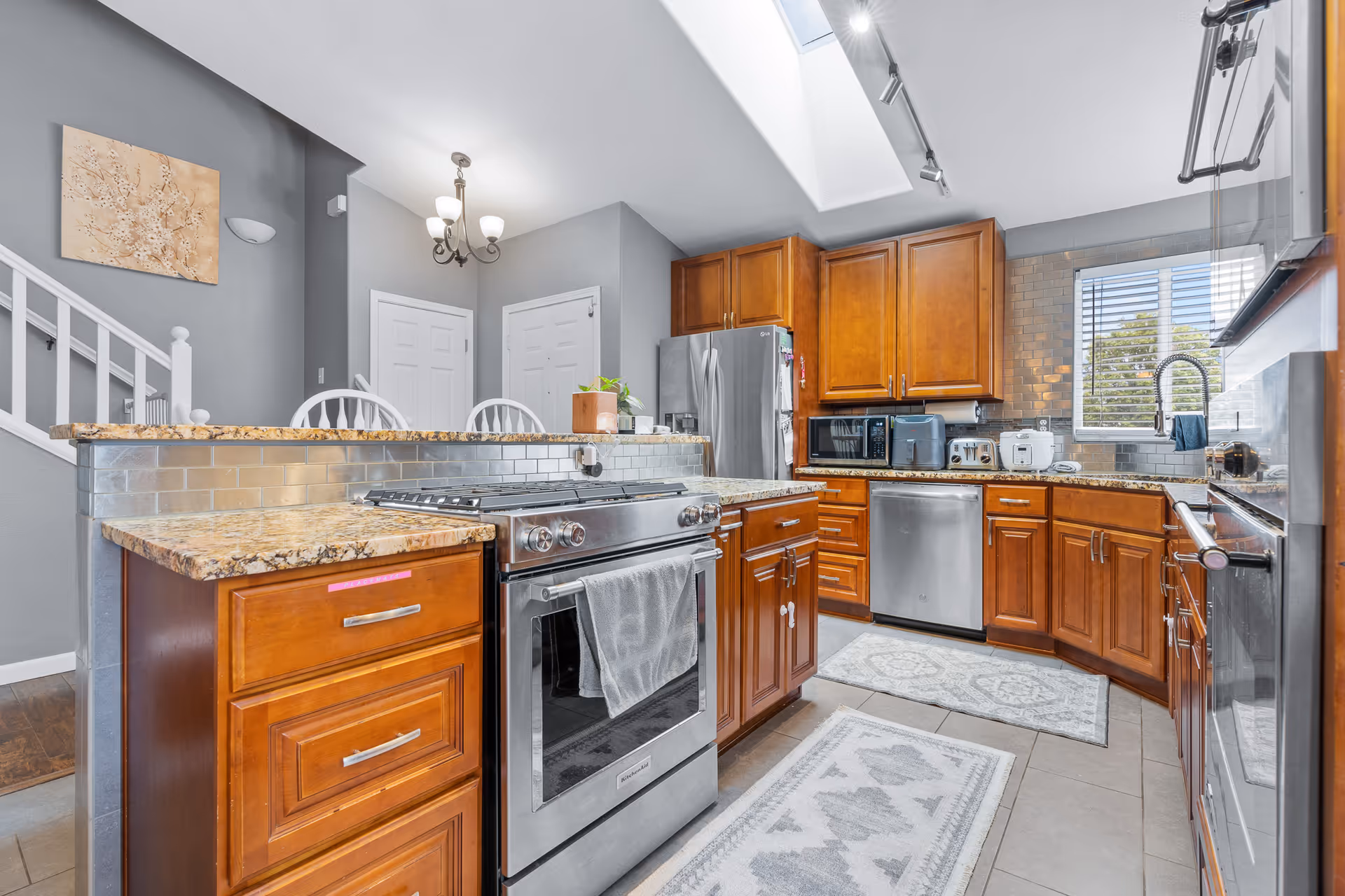 Modern kitchen with wooden cabinets, granite countertops, stainless appliances, bar seating, and skylight.