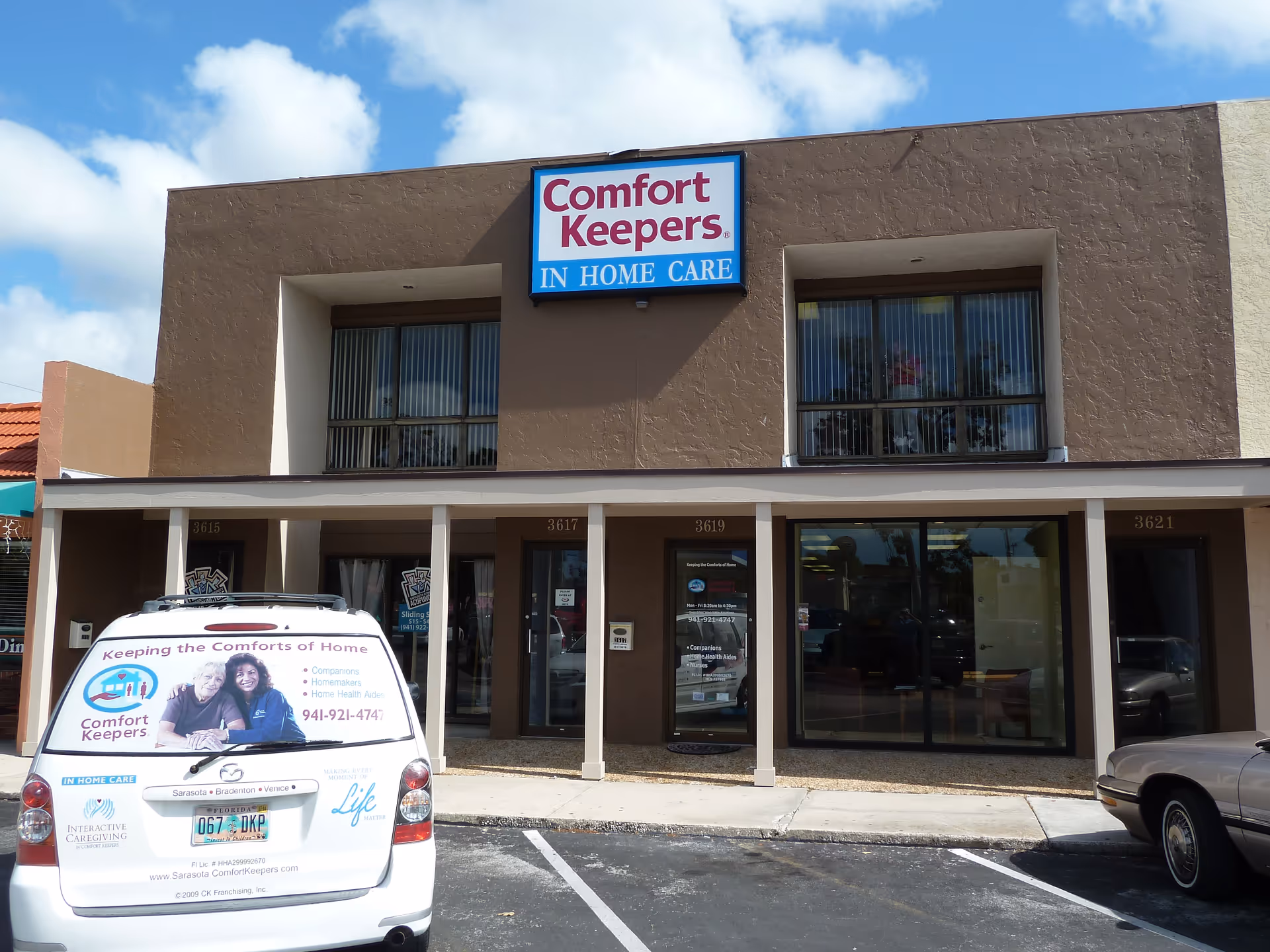 Front of Comfort Keepers building with sign, storefront windows, and a parked van.