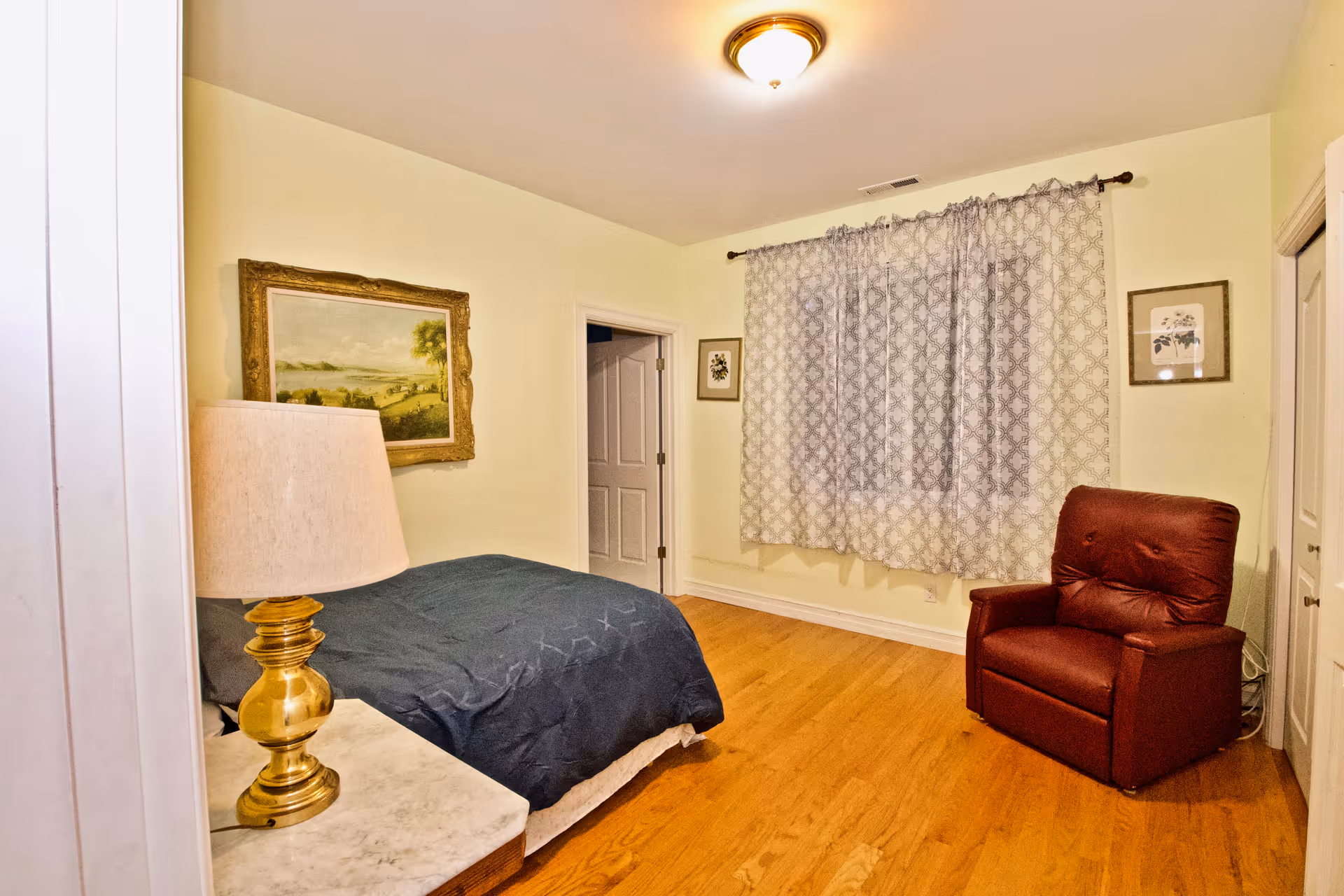 Cozy bedroom with a bed, lamp, curtains, and a burgundy armchair.