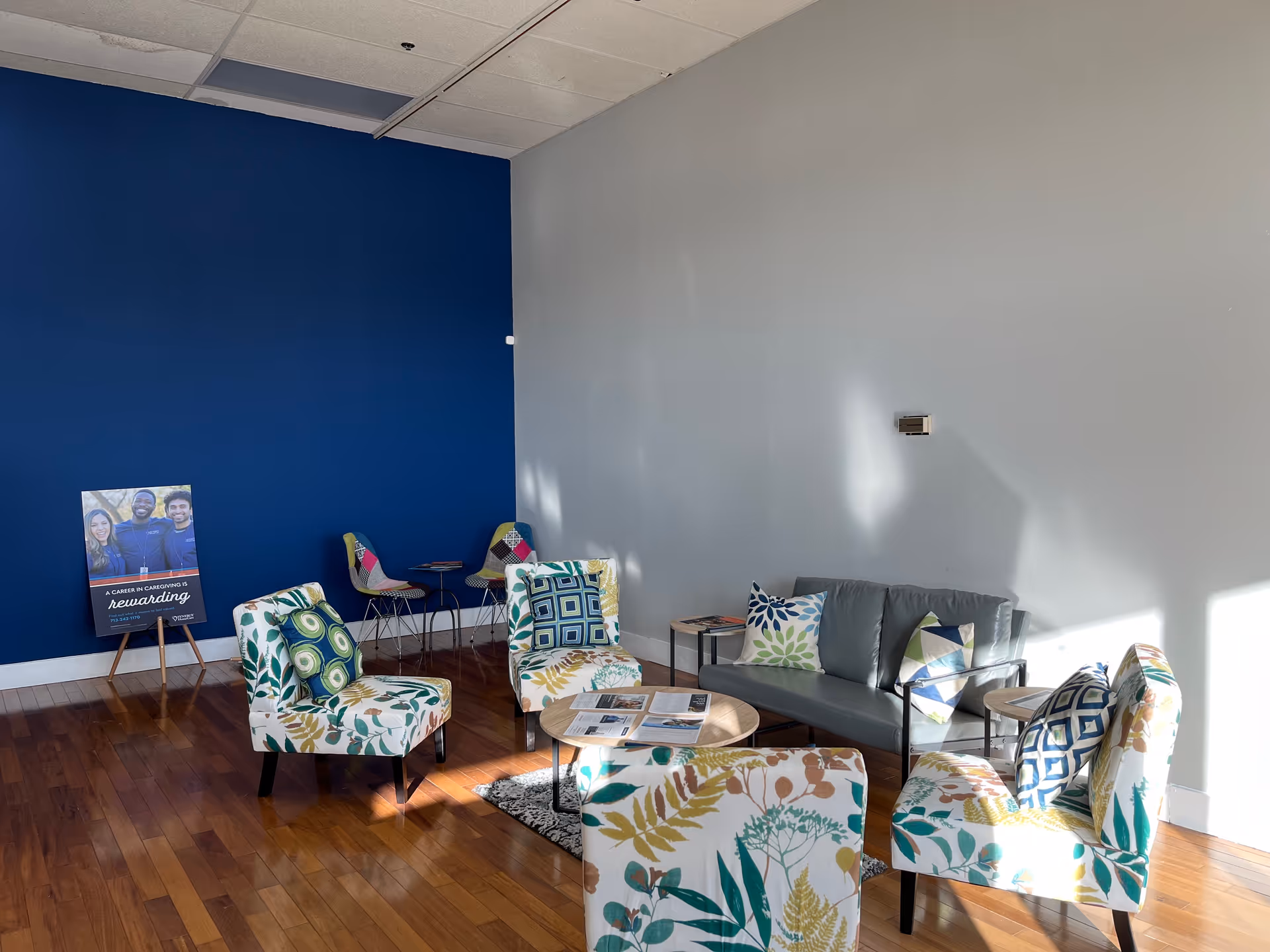 Bright lounge area with blue wall, patterned chairs, sofa, and wooden floor.