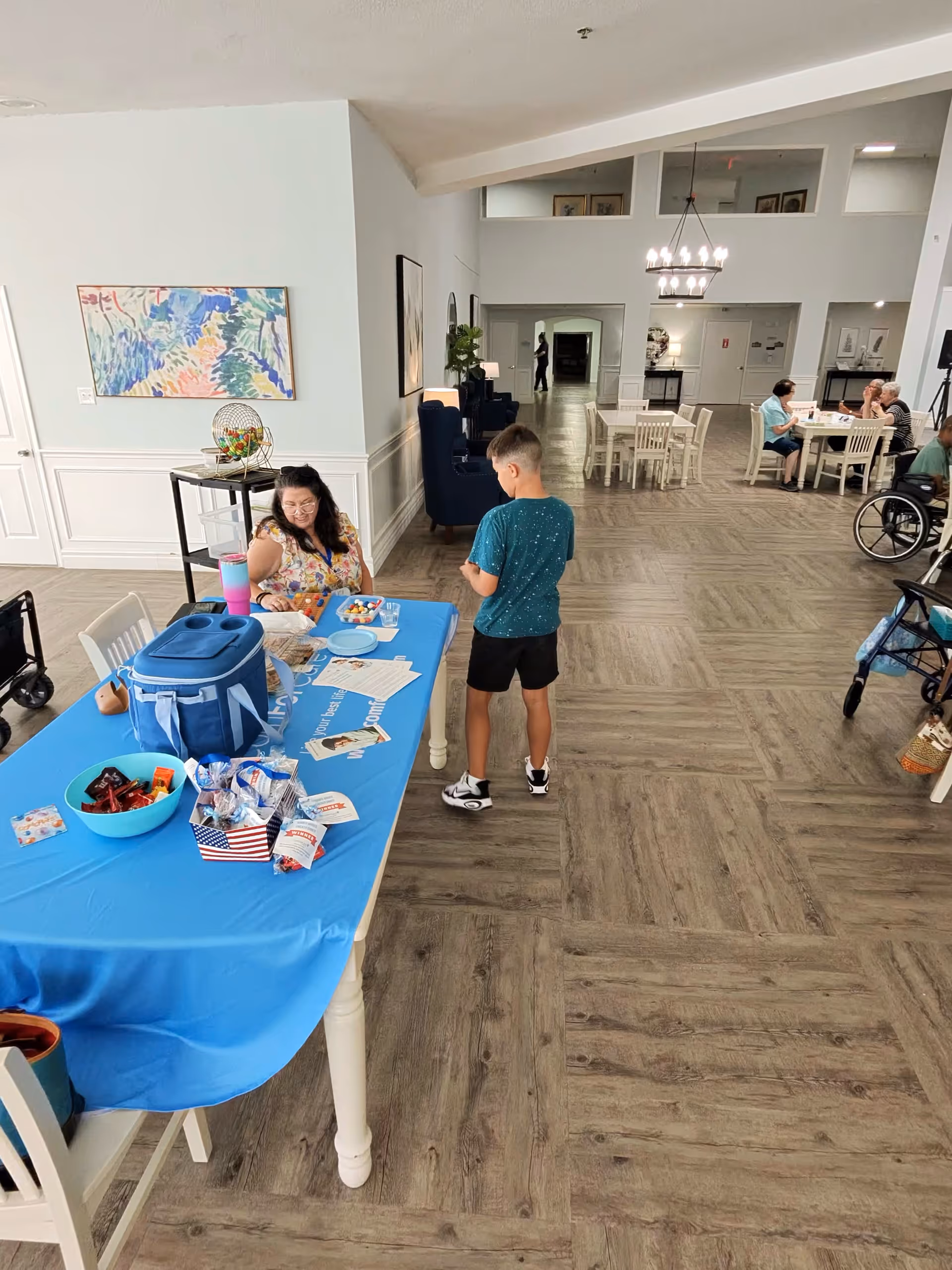 Bright senior living common area featuring a long blue table and group of people.