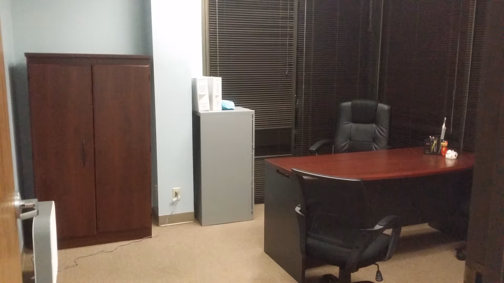 Office in a senior living facility with desk, chairs, a cabinet, and blinds.