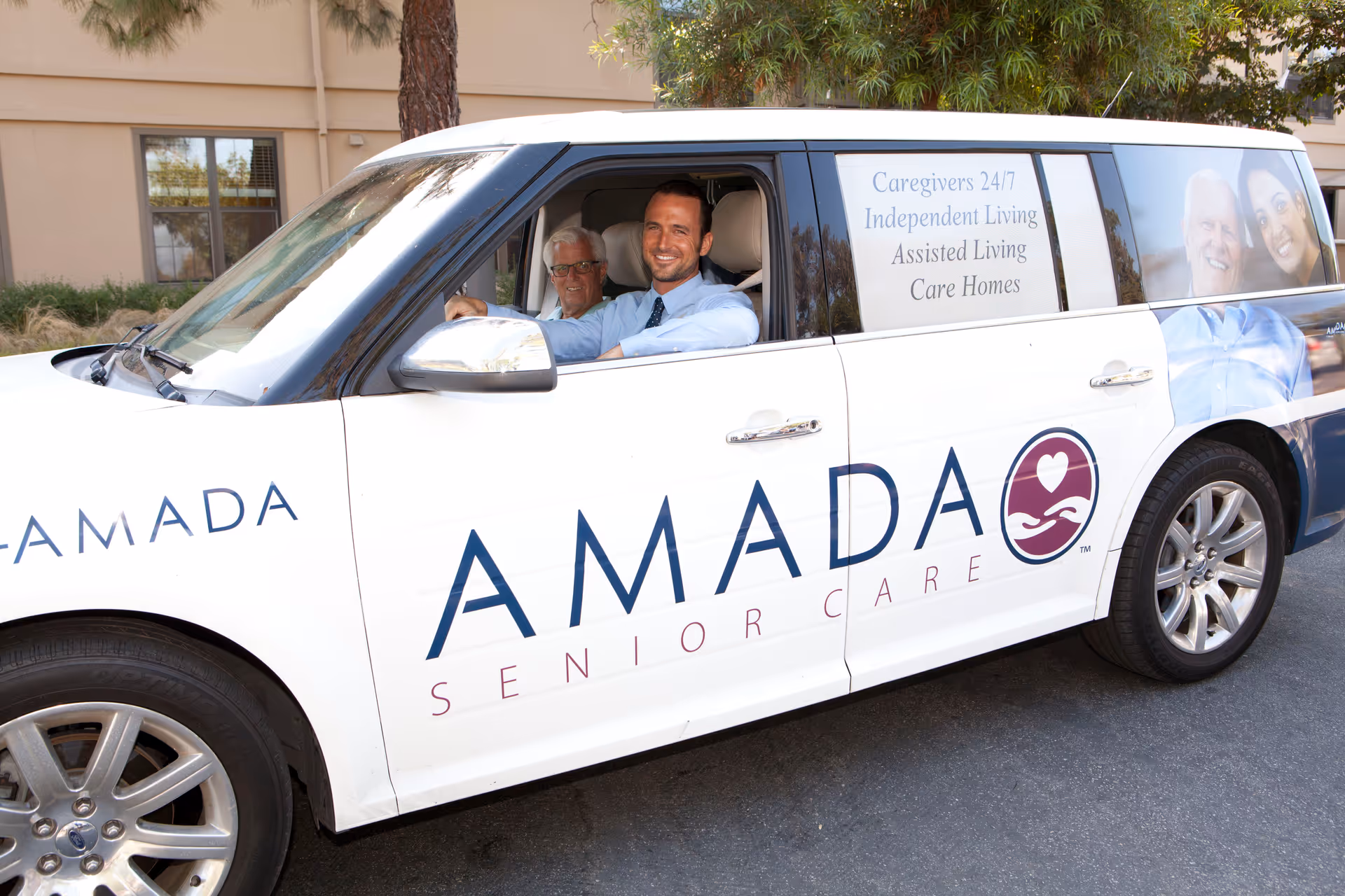 White Amada Senior Care van with two people in the driver's and passenger seats.