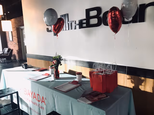 Reception table with BAYADA branding, balloons, and gift bags in a modern lobby.