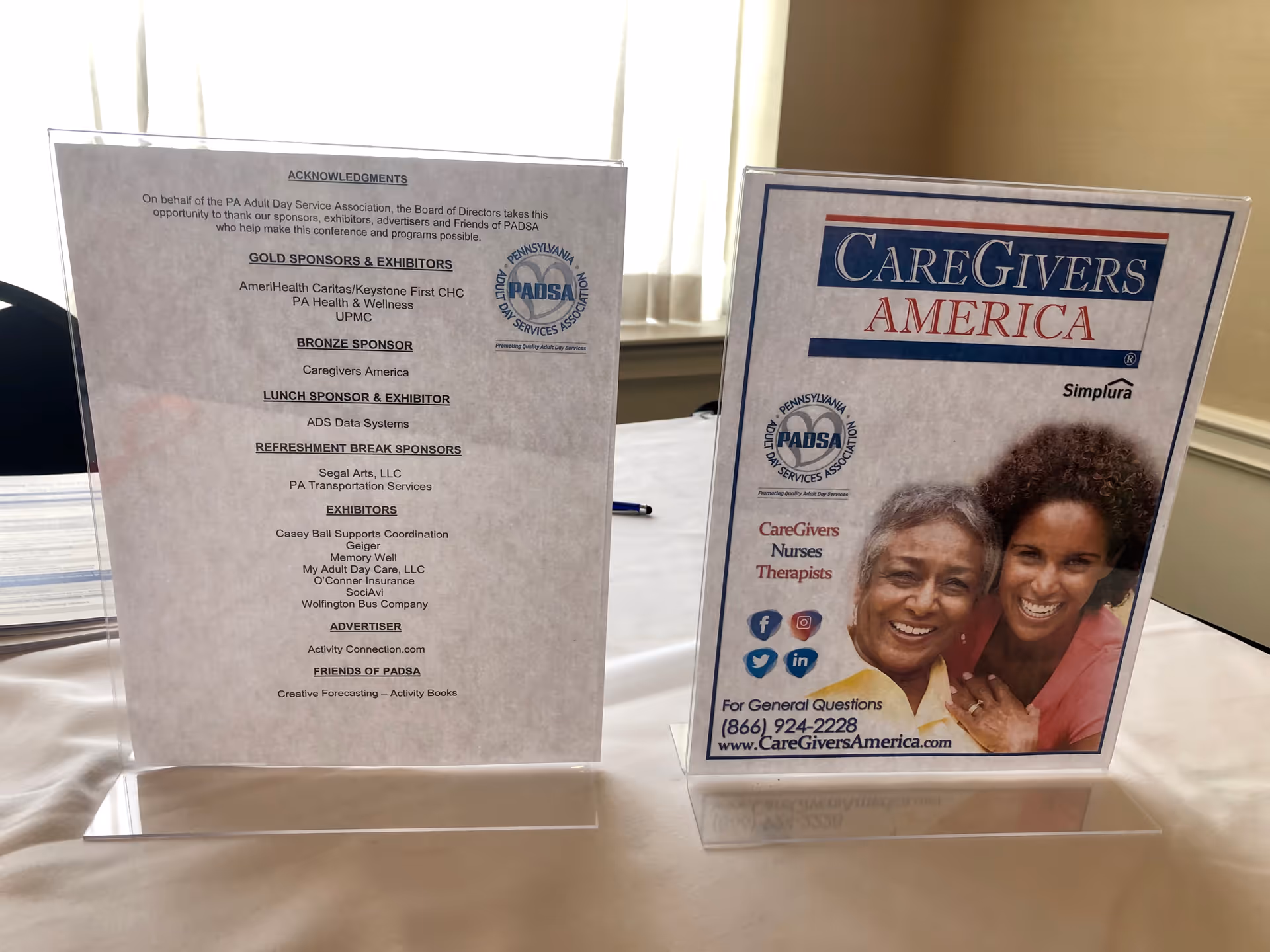 Two display boards on a table inside a room, one branded CareGivers America with a photo.