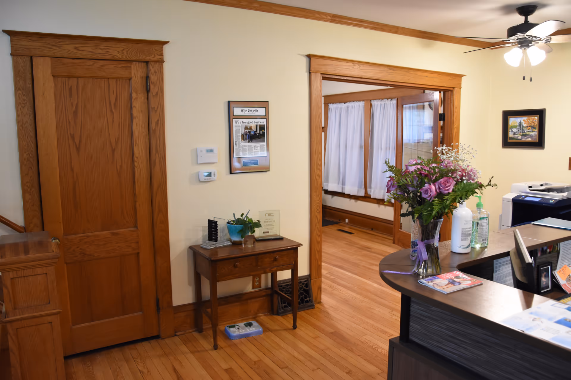 Reception area of a senior living facility with a desk, flowers, and wooden doors.
