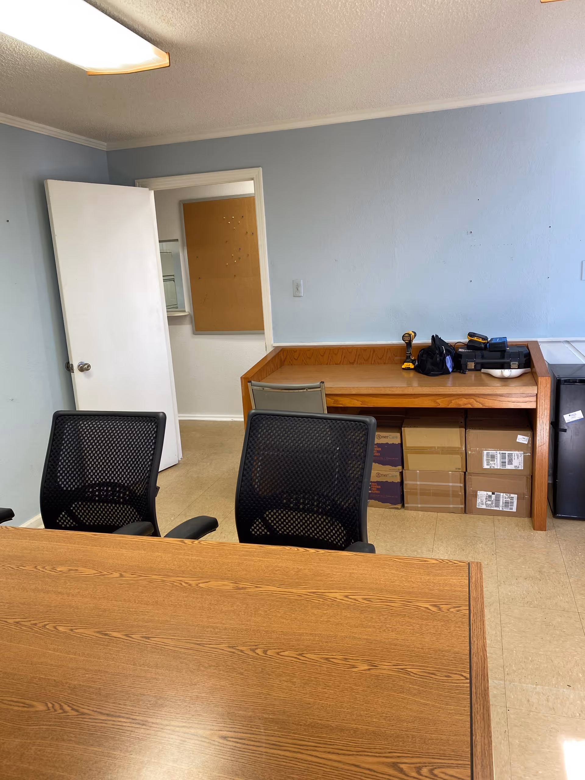 Office-like room with a wooden conference table, black chairs, and a desk against a blue wall.