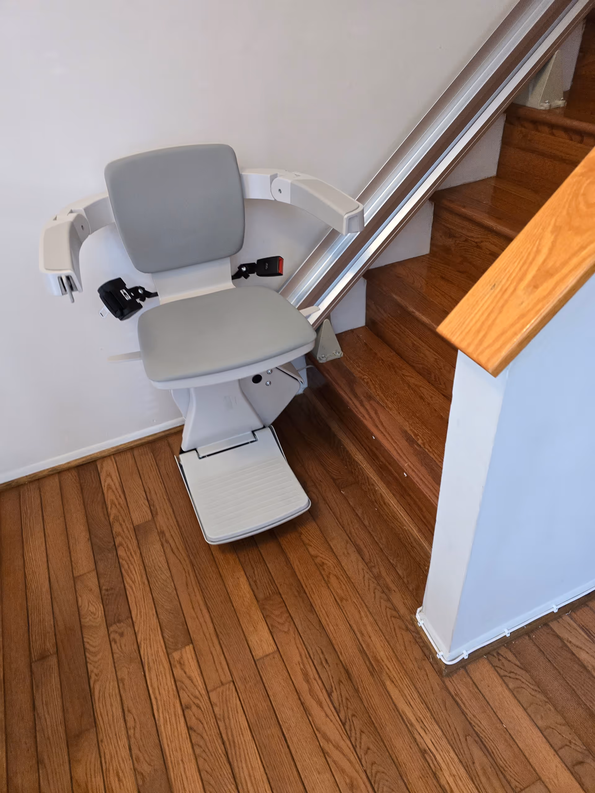 Indoor stairlift chair mounted on a wooden staircase beside a white wall.