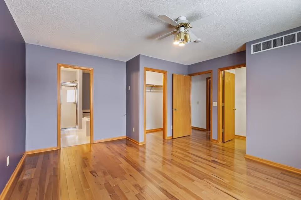 An empty room with purple walls, hardwood floor, and multiple doorways.