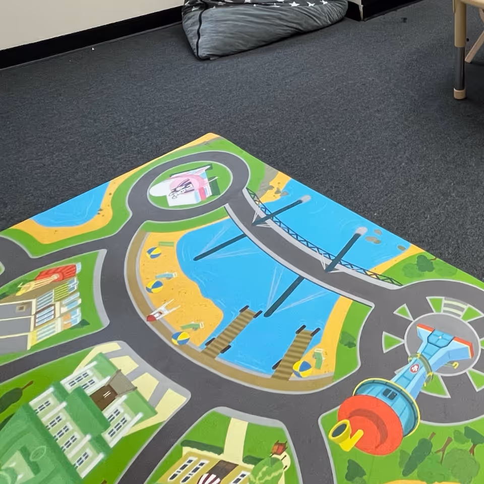 Colorful children's play mat with roads and buildings on a blue carpet in a room.