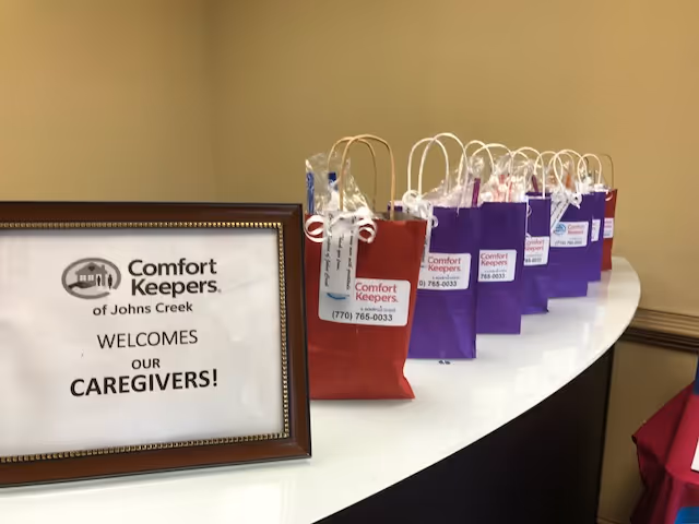 Framed sign reading Welcome caregivers and a row of gift bags on a curved white table.