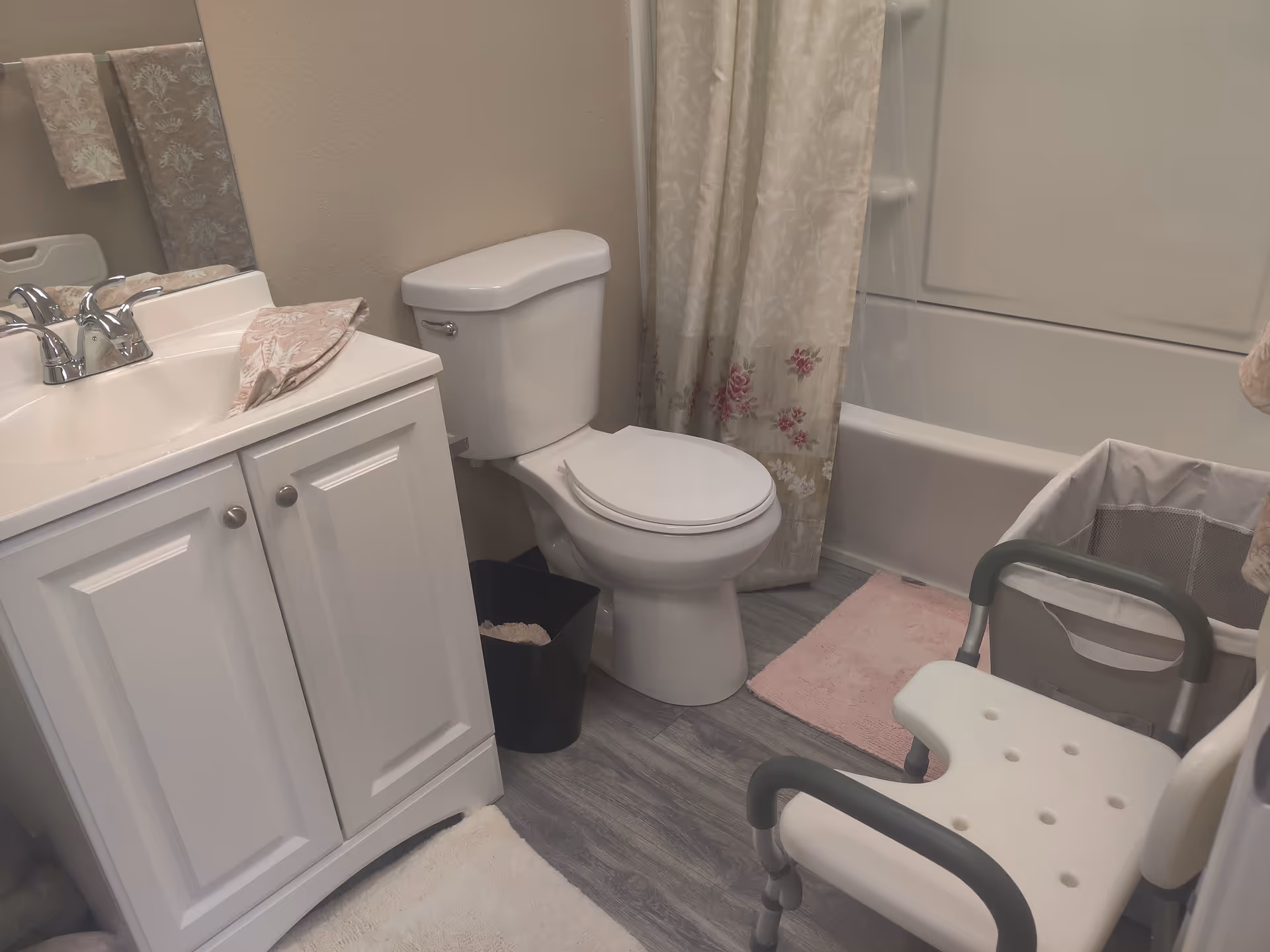 Bathroom in senior living unit with sink, toilet, bathtub, shower curtain, and transfer chair.