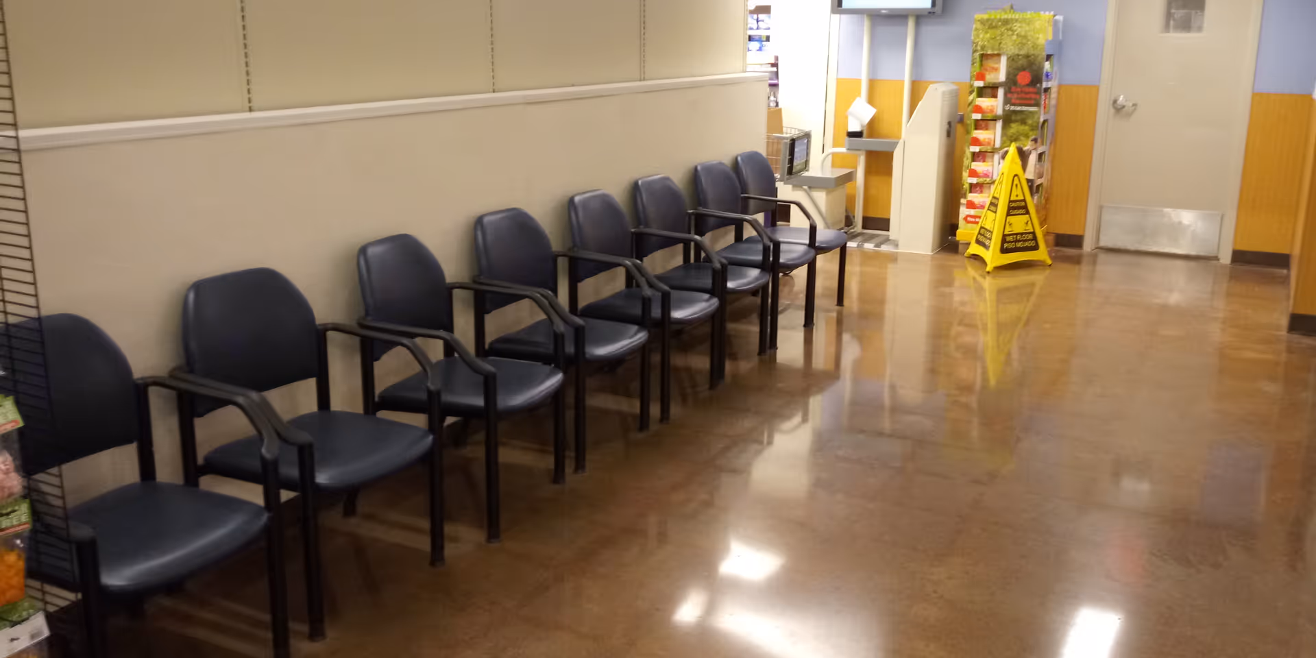 Row of navy blue chairs along a beige wall in a quiet Kroger Pharmacy waiting area.