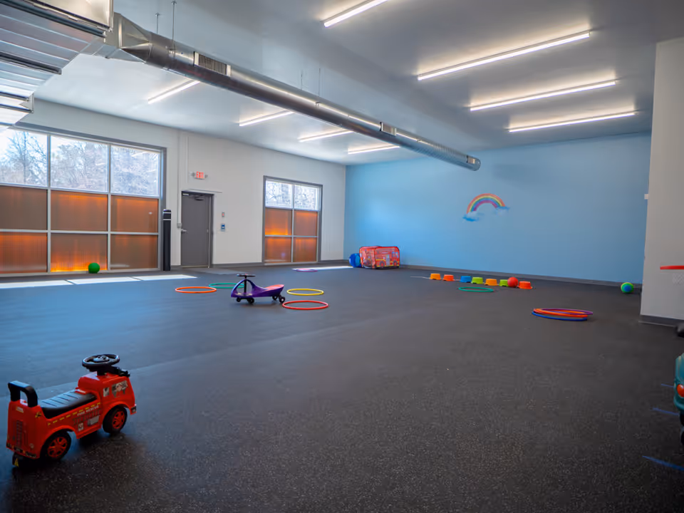 Spacious indoor playroom with blue wall, rainbow mural, and scattered children's toys.