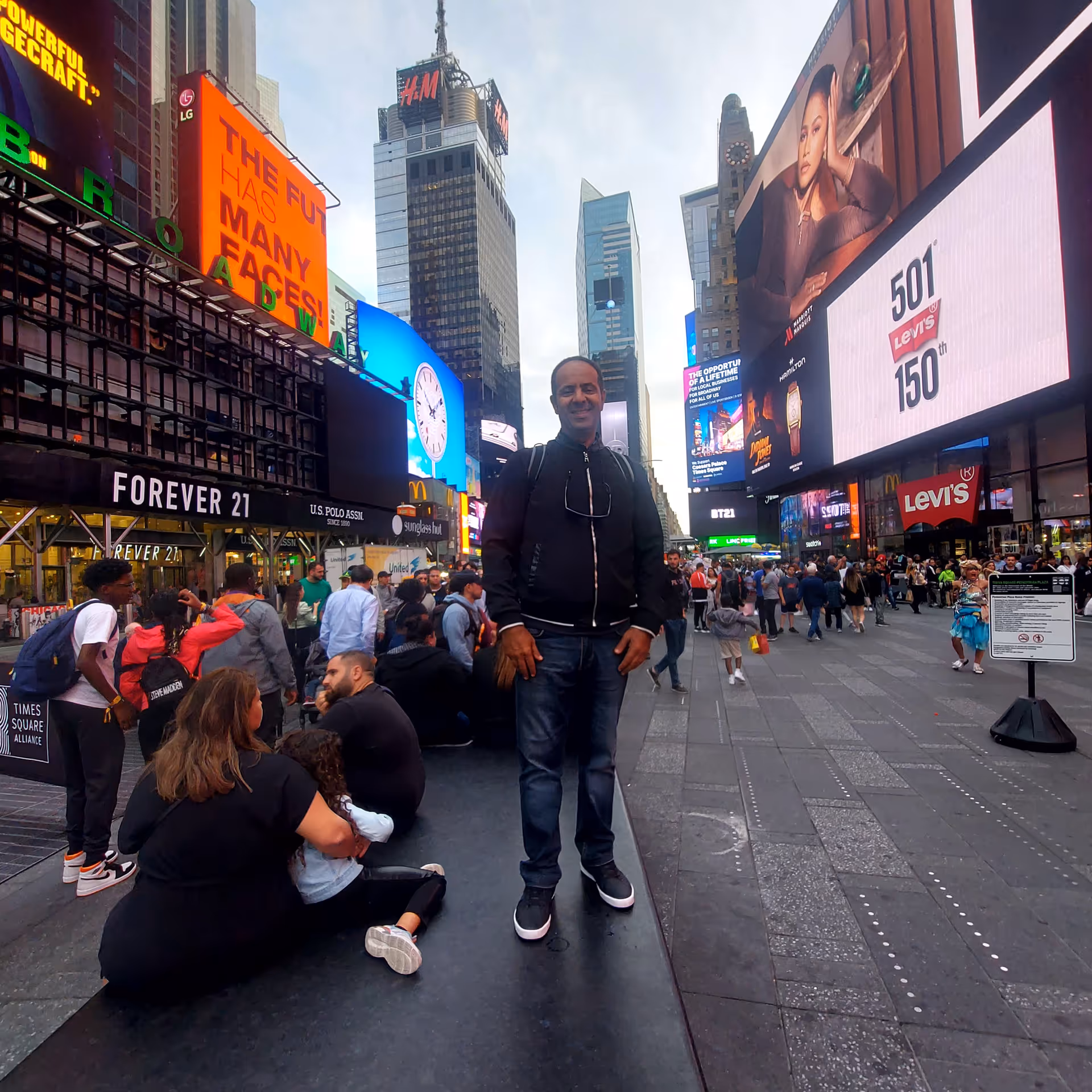 A man stands in busy Times Square among large digital billboards and crowds.